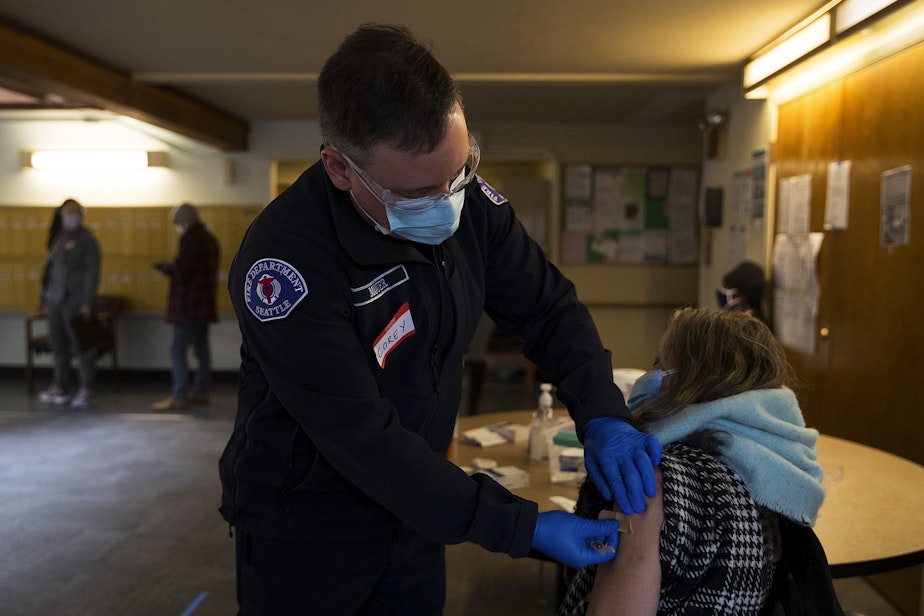 caption: Corey Mouer, a member of the Seattle Fire Department's mobile vaccination team, left, puts a bandaid on Jennifer Hamilton's arm after administering the first dose of the Moderna Covid-19 vaccine during a vaccine clinic in partnership with Seattle Housing Authority, on Tuesday, January 26, 2021, at Columbia Place on Holly Street in Seattle. 