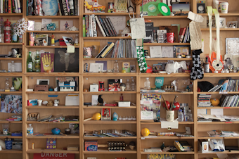 caption: The bric-a-brac-stacked shelves of the Tiny Desk.