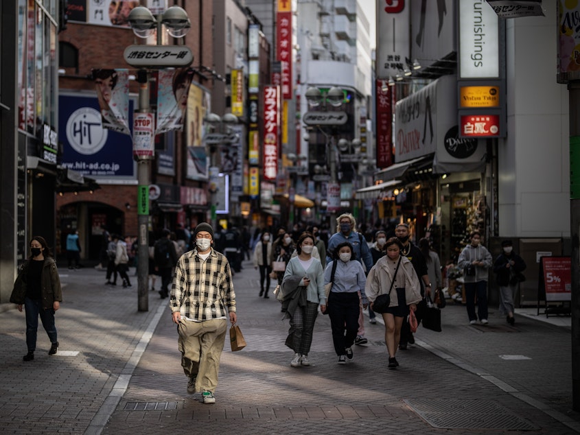 caption: A man wearing a face mask walks along a shopping street on March 25, 2022, in Tokyo.
