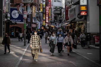 caption: A man wearing a face mask walks along a shopping street on March 25, 2022, in Tokyo.