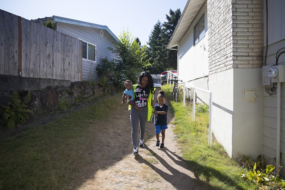 caption: Tiffany Montgomery walks to the overnight daycare facility to drop off two of her sons, 10-month-old Avalon Brown, left, and 5-year-old Curtis Brown, right, before working the night shift on Thursday, August 1, 2019, in Renton. 