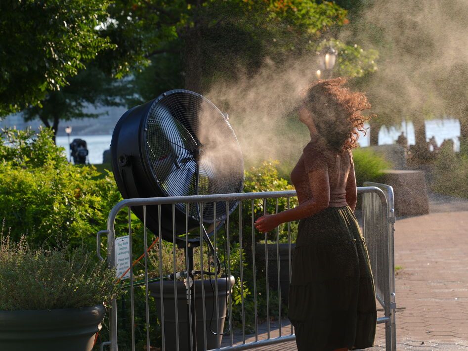 caption: A woman cools off near a water-spraying fan during a New York City heat wave in July 2024. Heat broke records months in a row around the planet between 2023 and 2024.