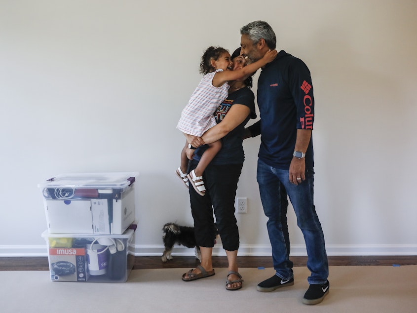 caption: During the pandemic, the number of young children in urban U.S. counties saw significant declines. Joyce Lilly, center, holds her granddaughter Paige alongside her husband, Anil, at their new home in July 2020 in Washingtonville, N.Y.