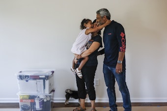 caption: During the pandemic, the number of young children in urban U.S. counties saw significant declines. Joyce Lilly, center, holds her granddaughter Paige alongside her husband, Anil, at their new home in July 2020 in Washingtonville, N.Y.