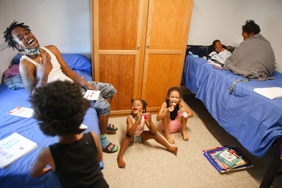 caption: Gregory Wraggs Sr. laughs with his daughters Av-ai, 5, left, Analiyze, 4, center, and Alycia, 8, as they eat jello, and his wife Shadoria Wraggs, right, plays with their two-month-old son Gregory Jr. inside their temporary room at the King County Cooling Center in White Center, Monday, June 28. The family has been living in their van for the past year and were able to stay in an air-conditioned unit at the cooling center this week as temperatures rose into the 100s.