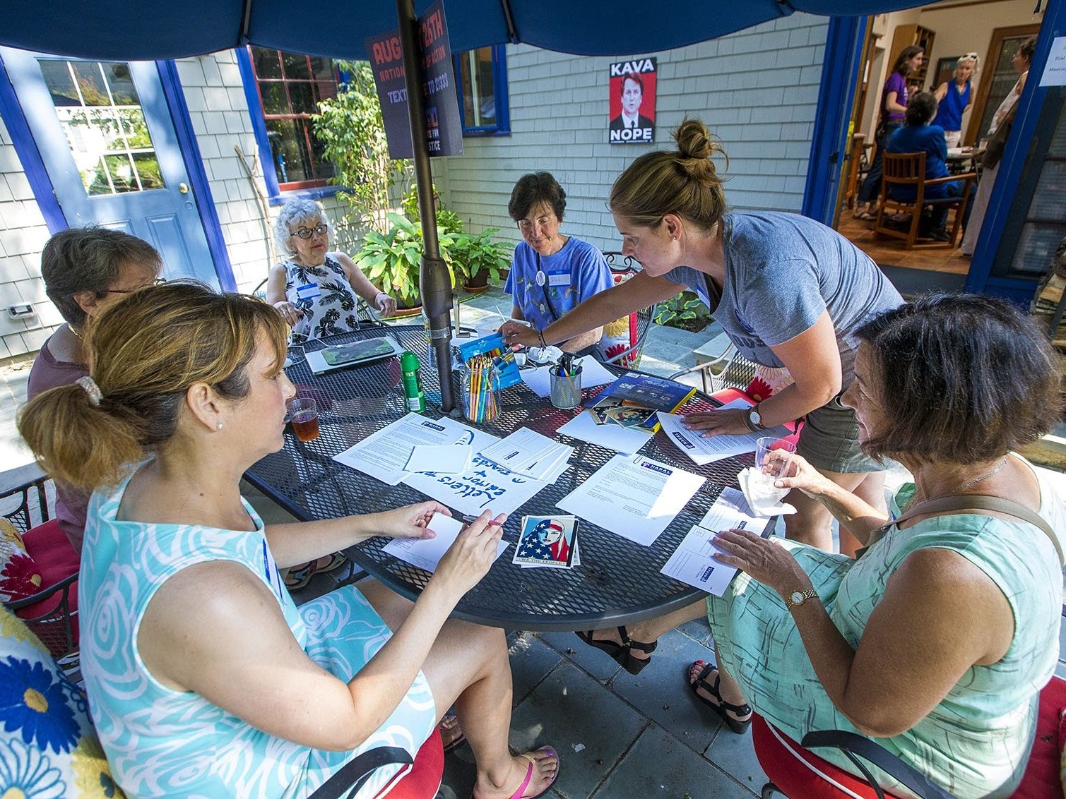 caption: A group of NARAL volunteers sit around a table writing letters and postcards to senators and news outlets around the country protesting the nomination of Judge Brett Kavanaugh to the Supreme Court.