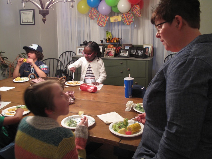 caption: Foster parent Mary Pico (right) eats dinner with her children and others gathered at her home for a monthly meeting of families in the Mockingbird Family Model of foster care.