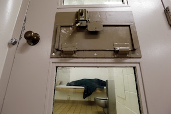 caption: An inmate huddles under a heavy blanket on a bunk in the psychiatric unit of the Pierce County jail in Tacoma, Wash. in 2014.