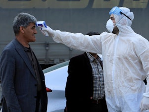 caption: As the coronavirus that causes COVID-19 spreads to more areas, a health worker checks  a man's temperature at a checkpoint in the outskirts of Duhok, Iraq, on Tuesday.
