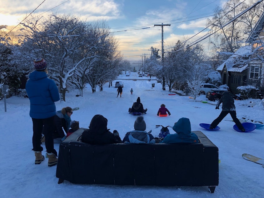 caption: Sean Eley, Renee Grazer and Gabe Goldman set up a couch to sip coffee and watch their kids sled down Juneau in West Seattle.
