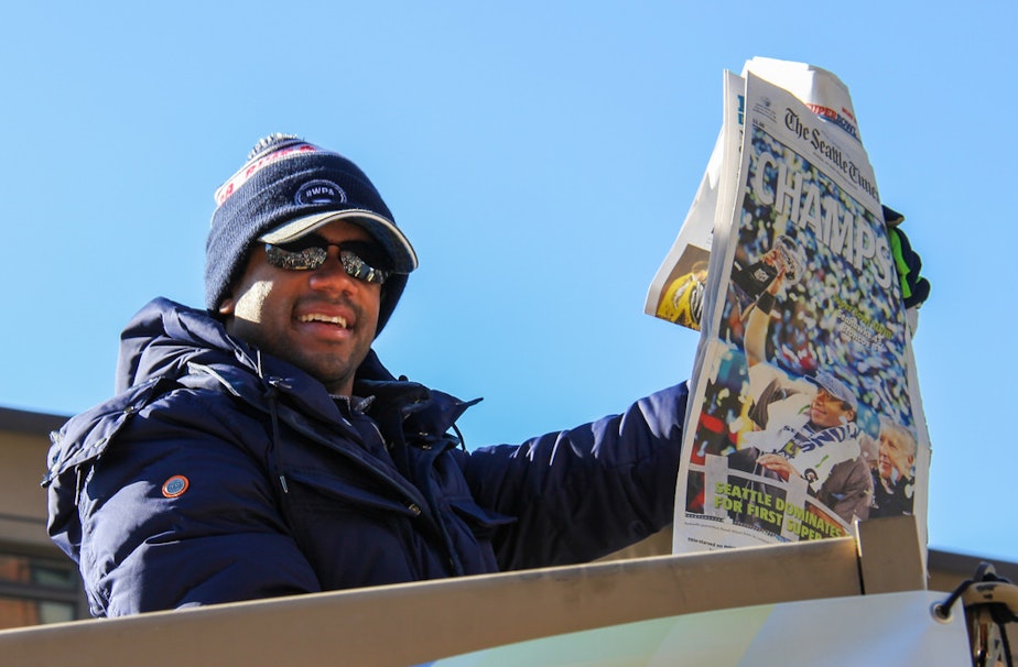 caption: Seattle Seahawks quarterback Russell Wilson holds up the frontpage proclaiming their championship during a post-Super Bowl rally in February.