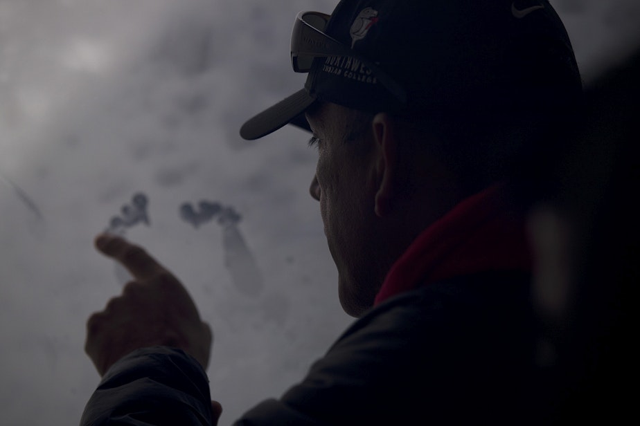 caption: Lummi Tribal Chairman Jay Julius uses the side of his fist and index finger to make what looks like feet on a window aboard King County Research Vessel SoundGuardian on Wednesday, April 10, 2019, after in the waters west of Bellingham. Lummi tribal members released one live chinook salmon into the Salish Sea on Wednesday as a spiritual offering to J17, an orca matriarch who has been ailing.