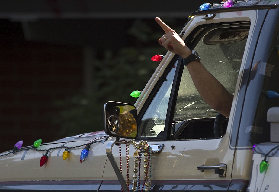 caption: Hank Lomasney points to Wallingford residents as they cheer for the Seattle Quarantine Parade on Friday, May 8, 2020, in Seattle.
