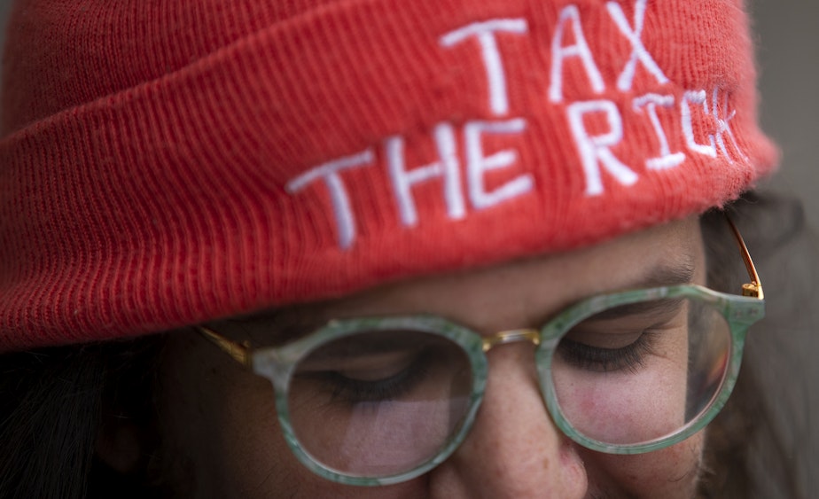 caption: Whitney Kahn attends an "All Together for Seattle Schools" rally wearing a hat that reads "tax the rich" ahead of a school closures meeting on Tuesday, May 28, 2024, at Roosevelt High School in Seattle. 