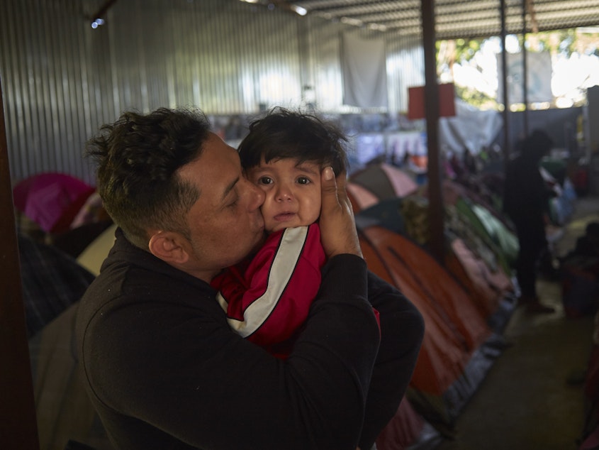 caption: Juan Carlos Perla of El Salvador kisses his 10-month-old son, Joshua, inside a migrant shelter in Tijuana, Mexico, where they await their asylum hearing in San Diego.