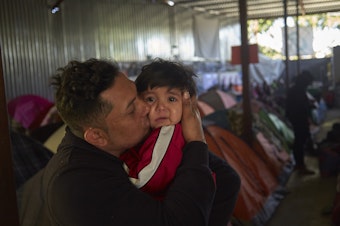 caption: Juan Carlos Perla of El Salvador kisses his 10-month-old son, Joshua, inside a migrant shelter in Tijuana, Mexico, where they await their asylum hearing in San Diego.