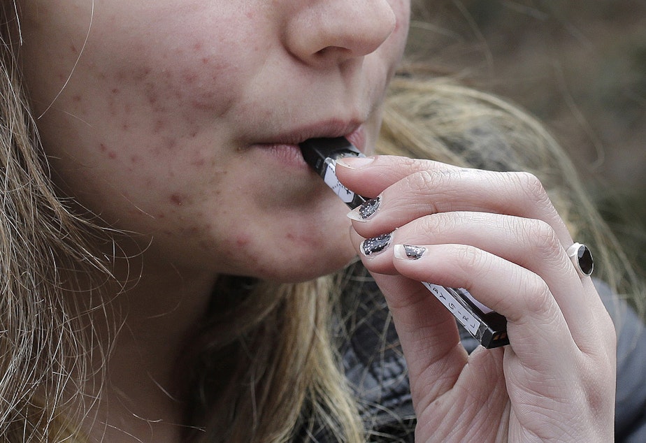 caption: In this April 11, 2018 file photo, a high school student uses a vaping device near a school campus in Cambridge, Mass. 