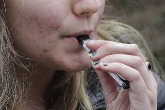 caption: In this April 11, 2018 file photo, a high school student uses a vaping device near a school campus in Cambridge, Mass. 