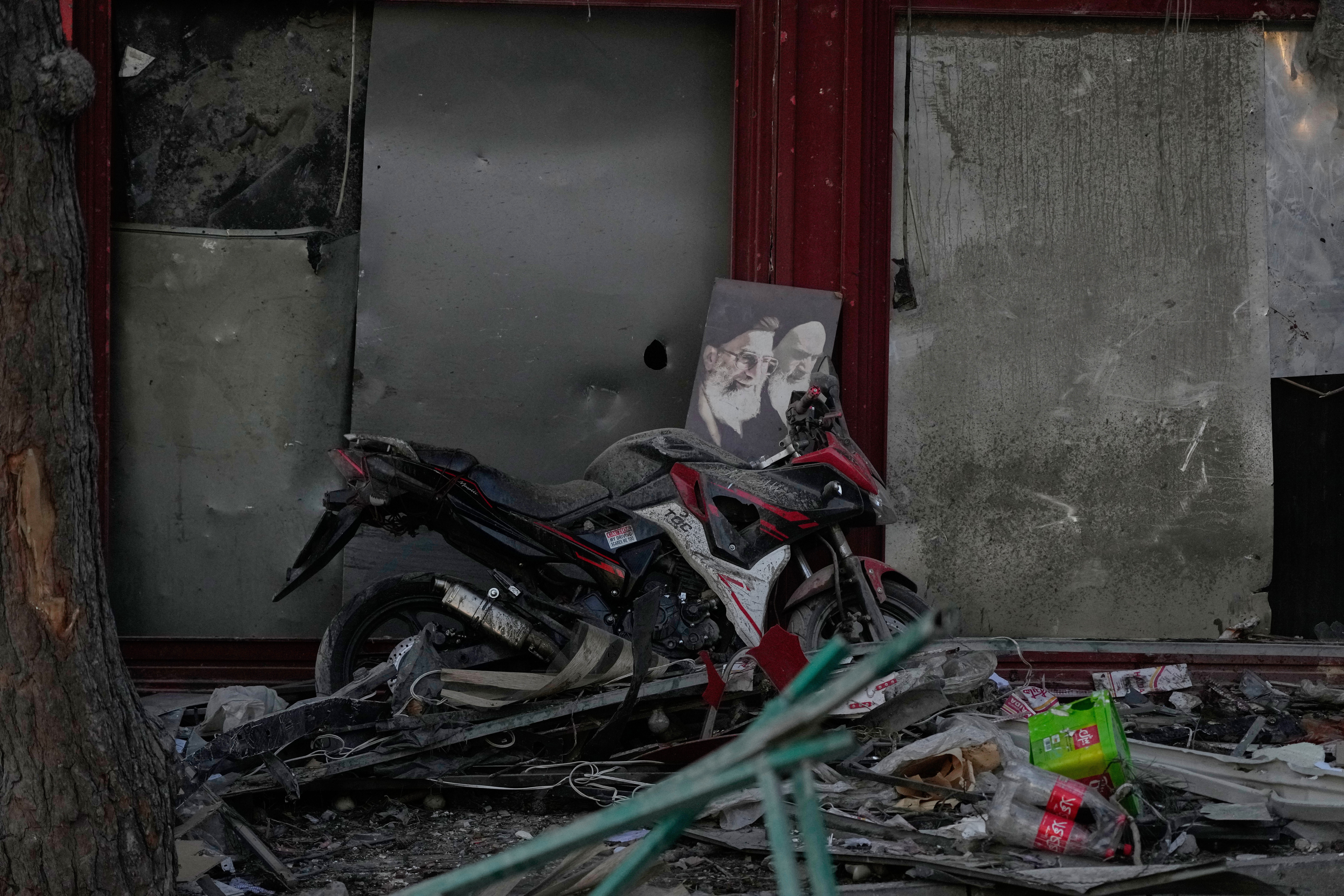 caption: A poster of the late Supreme Leader Ayatollah Ali Khamenei, who was killed during the ongoing joint U.S.-Israeli military campaign, and the late Iranian Revolutionary founder Ayatollah Khomeini, right, lays on a motorcycle amid debris left by a strike in Tehran, Iran, Monday, March 2, 2026. 