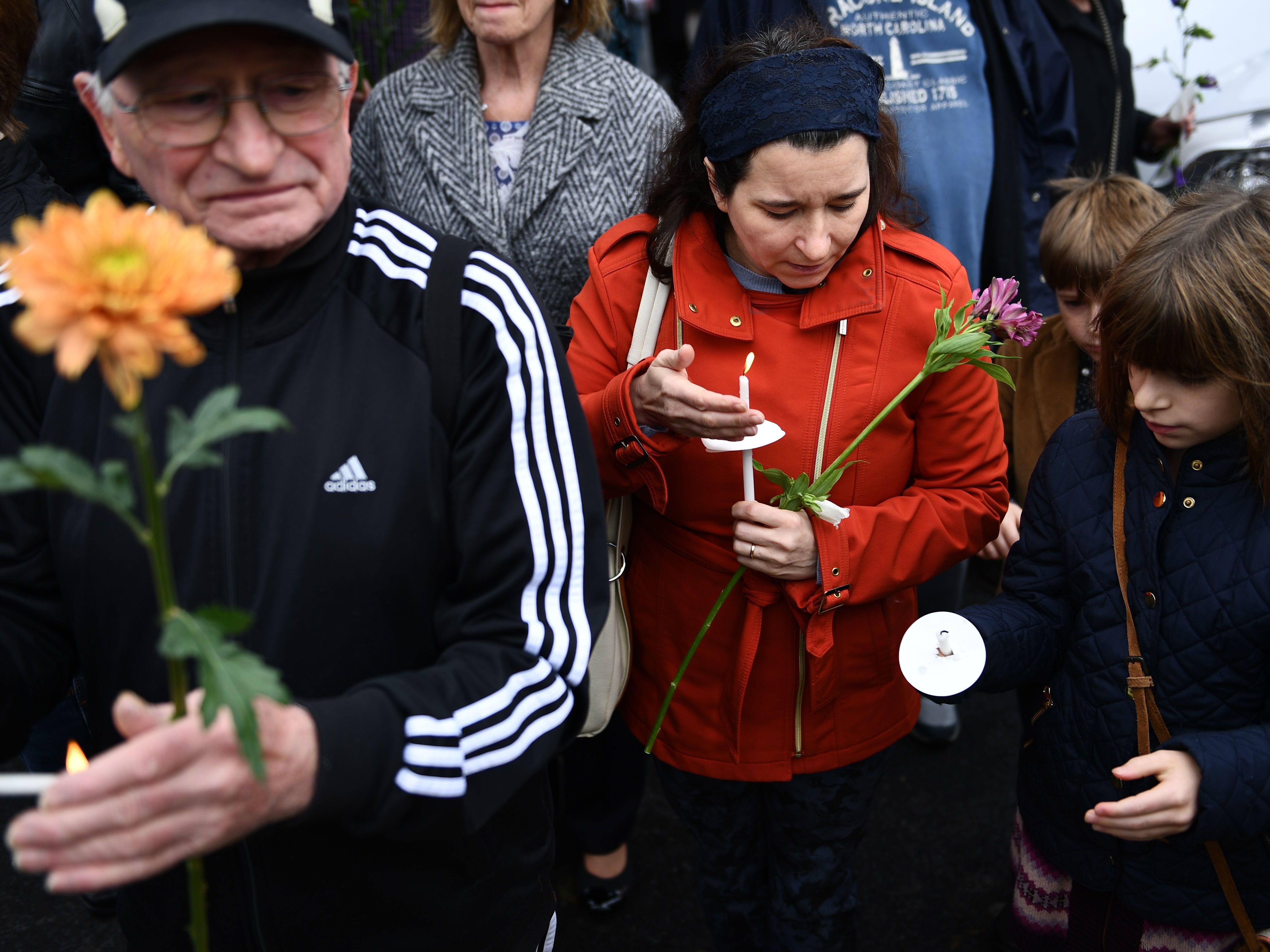 caption: People pay their respects in front of a memorial on Sunday outside of the Tree of Life synagogue in Pittsburgh after a shooting there on left 11 people dead.
