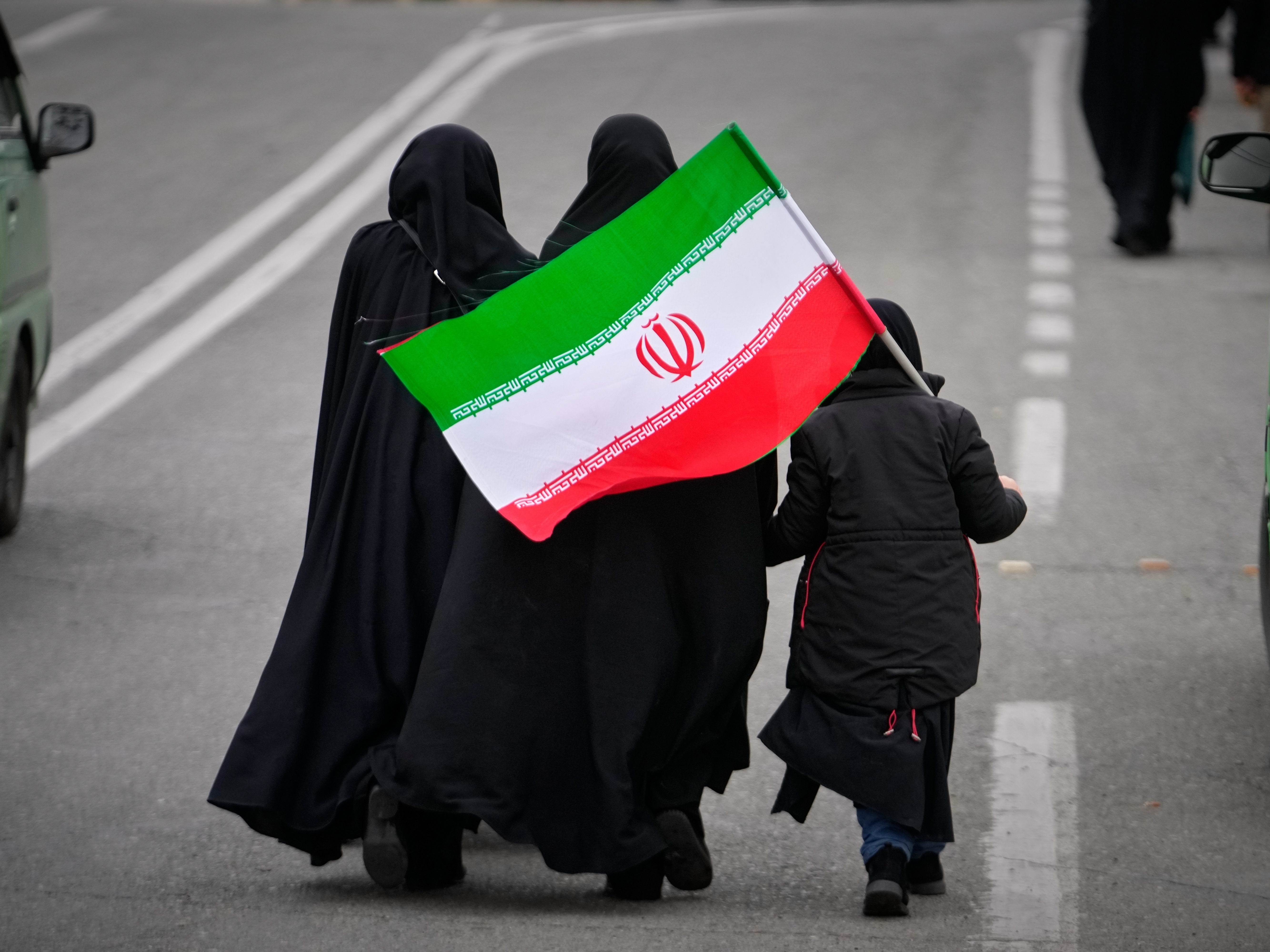 caption: Two women and a child holding an Iranian flag walk toward the Imam Khomeini Grand Mosque to attend Friday prayers in Tehran, Iran, on Friday.