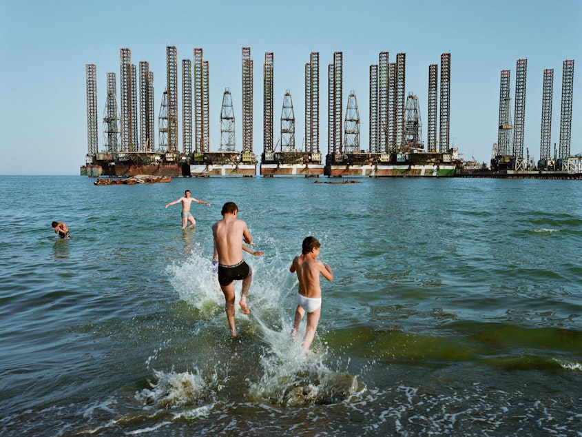 caption: Boys play in the water in front of offshore oil rigs at Sixov Beach, on the outskirts of the city. Baku, Azerbaijan, 2010.