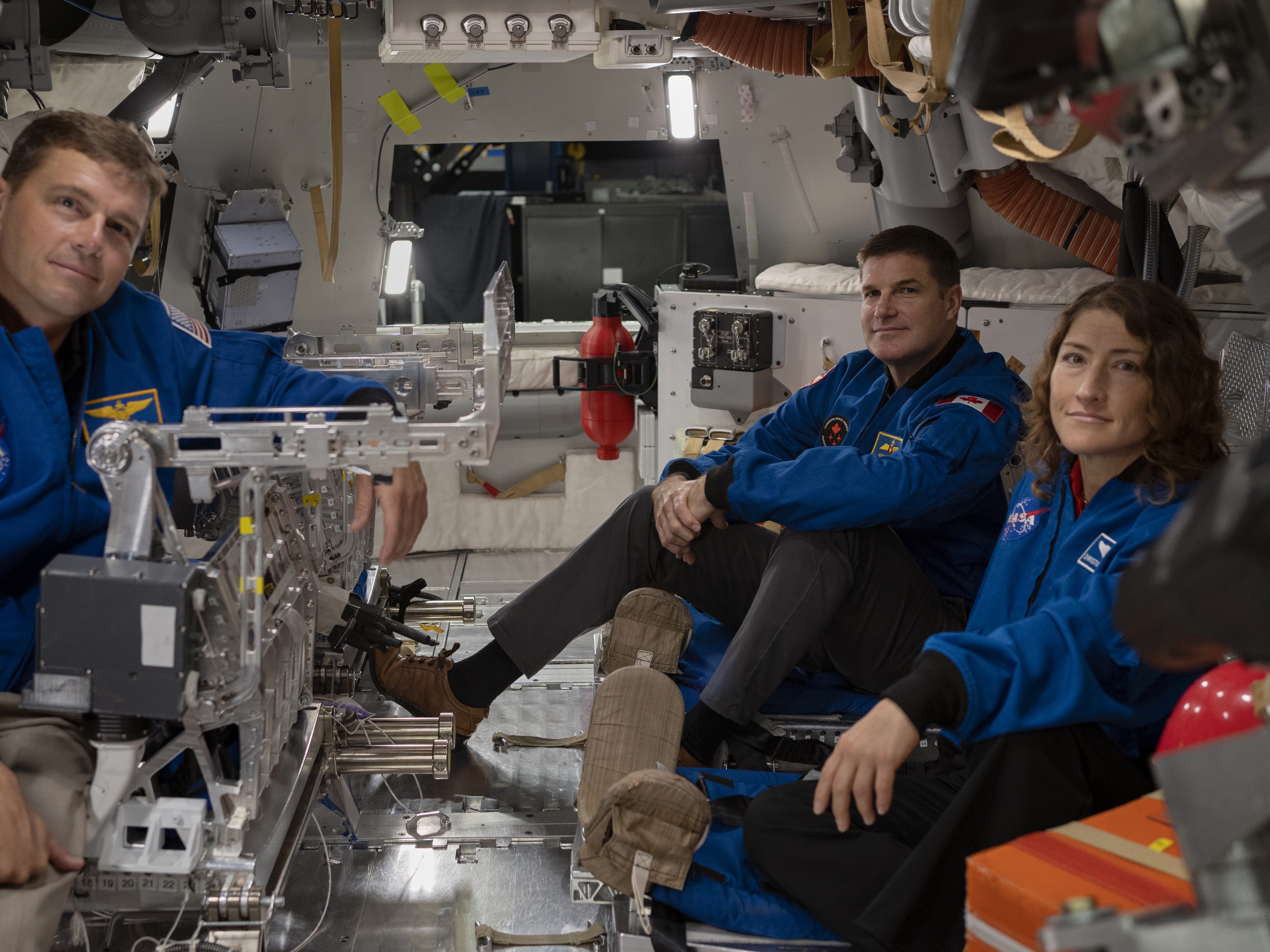 caption: From left to right: Astronauts Reid Wiseman, Jeremy Hansen and Christina Koch settle in inside the Orion spacecraft mockup.