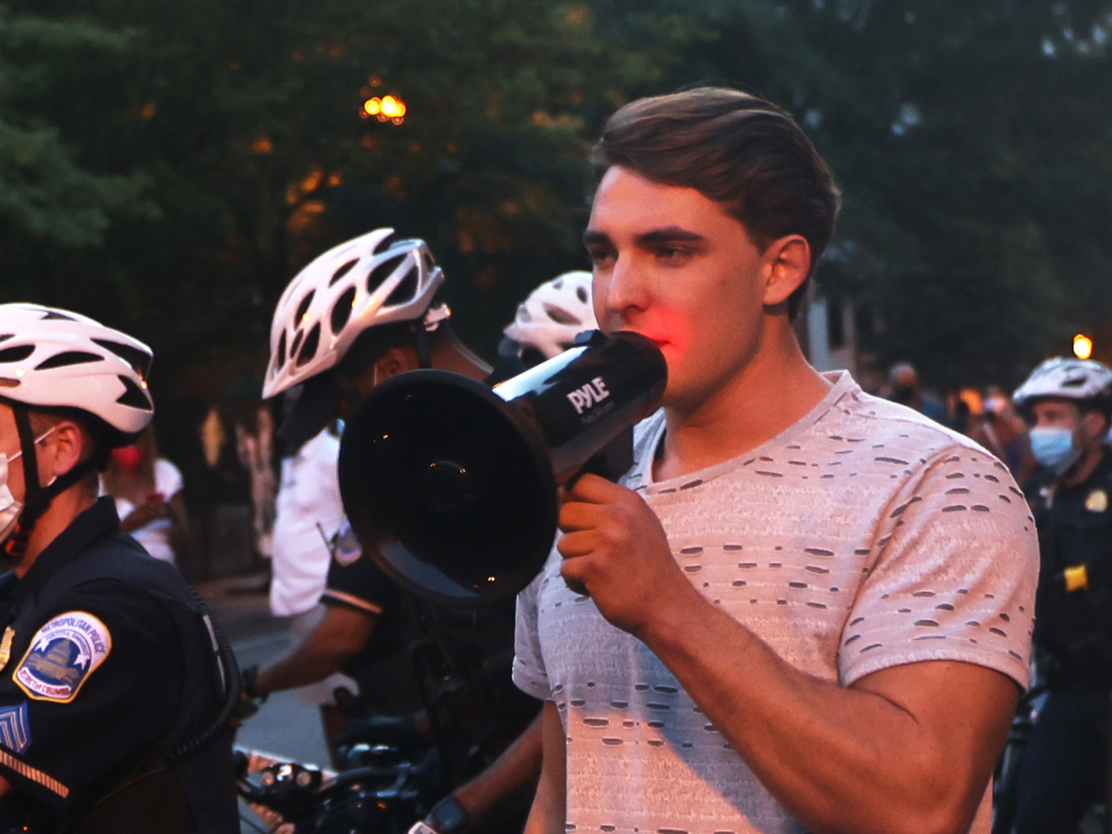 caption: Jacob Wohl, pictured here surrounded by police officers at a 2020 protest in Washington D.C., is one of two right-wing activists who were behind a 2020 robocall scheme that targeted minority voters. Wohl will now face probation, fines and 500 hours of voter registration assistance for pleading guilty to telecommunications fraud.