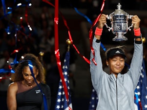 caption: Naomi Osaka of Japan poses with the championship trophy after winning the Women's Singles finals match against Serena Williams at the 2018 U.S. Open.
