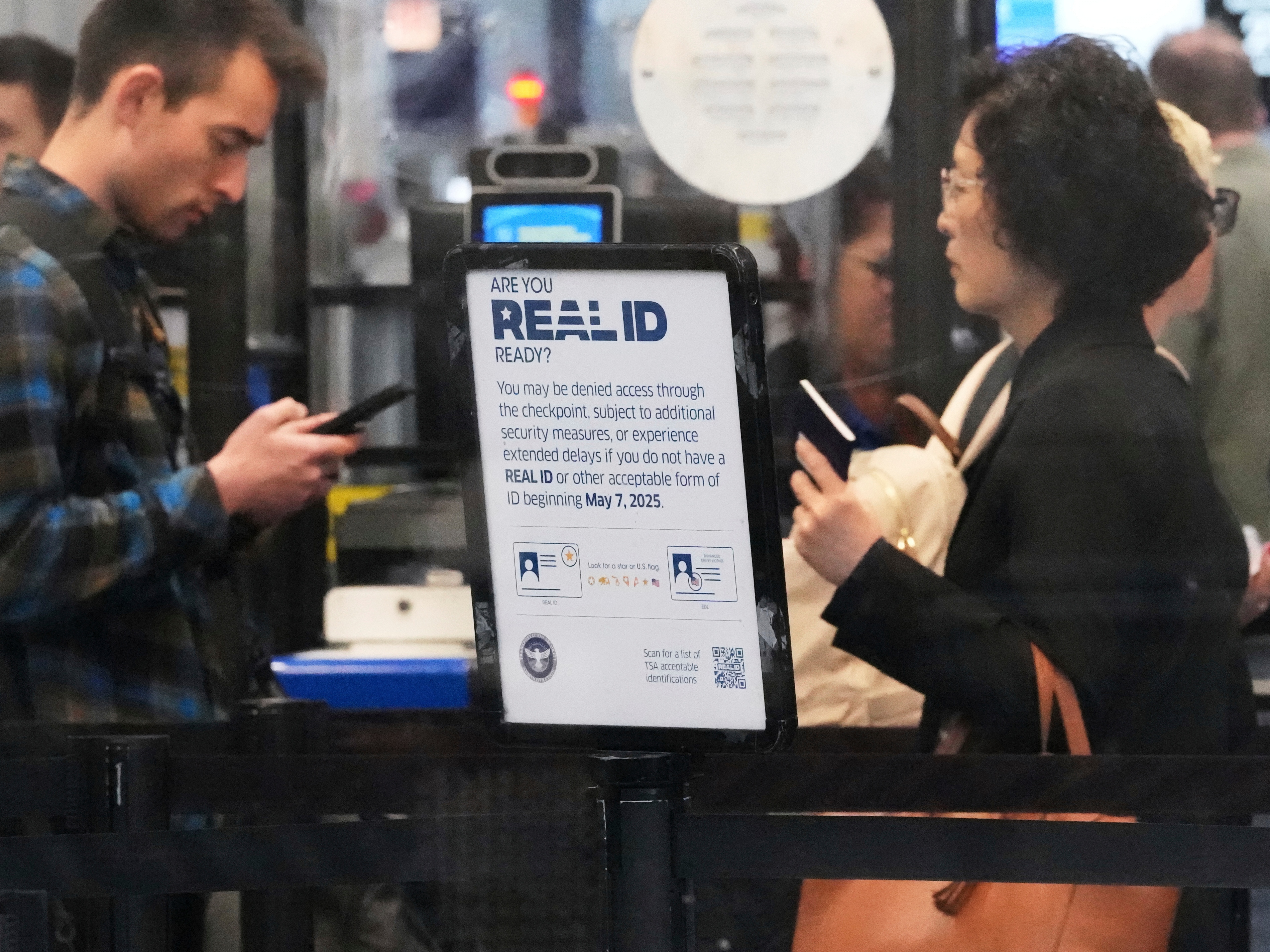 caption: A Real ID sign is displayed as travelers wait to go through security check point at O'Hare International Airport in Chicago, May 23, 2025.
