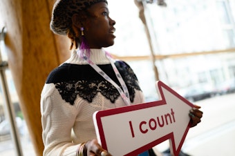 caption: Whitney Turner, an employee of the U.S. Census Bureau, holds an "I count" sign at a 2020 census advertising campaign event in Washington, D.C., in January 2020.