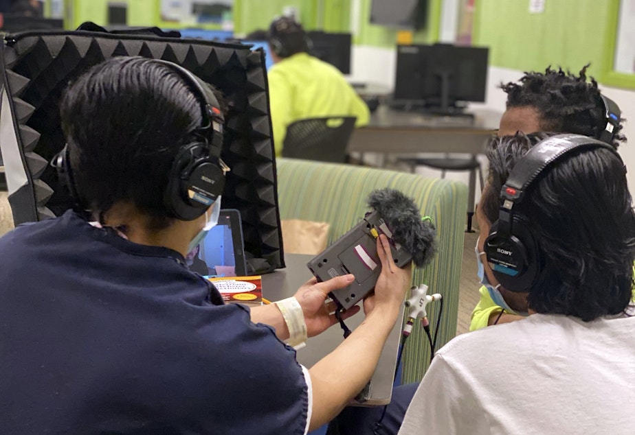 caption: Three teens get ready to record an interview in the library at the Judge Patricia H. Clark Children and Family Justice Center during a RadioActive podcasting workshop on April 15, 2021.