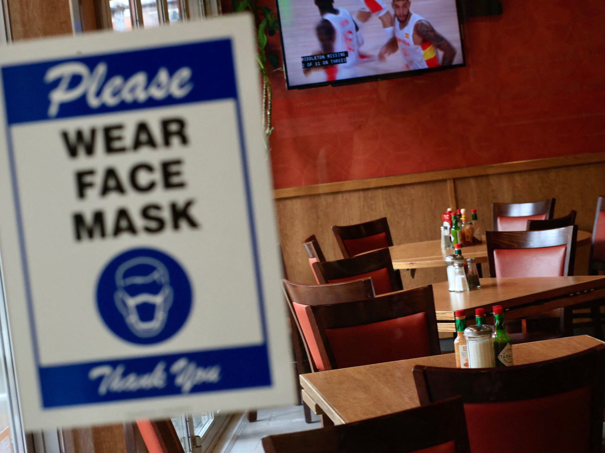 caption: A sign asking patrons to wear a mask is seen at the entrance of a restaurant in New York City on Aug. 3. The spread of the delta variant led to sharply slower economic growth in the July-to-September quarter.
