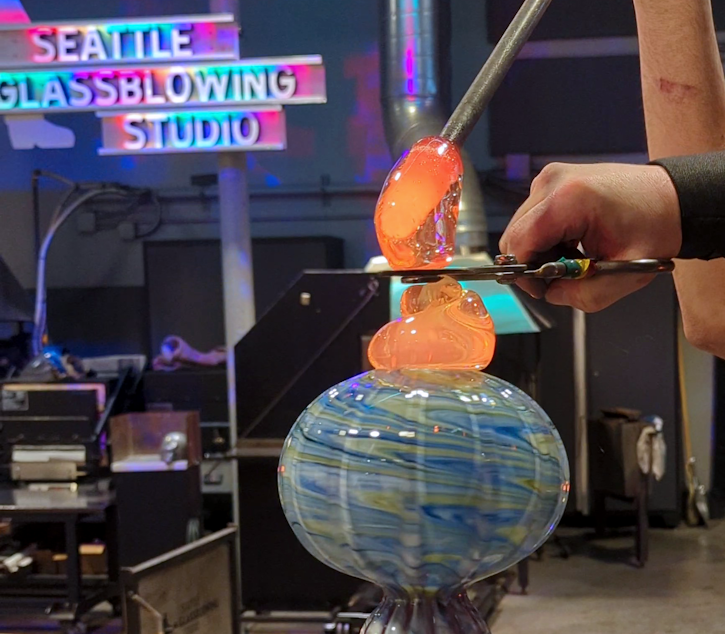 caption: A glassblower shapes their work at Seattle Glassblowing Studio.
