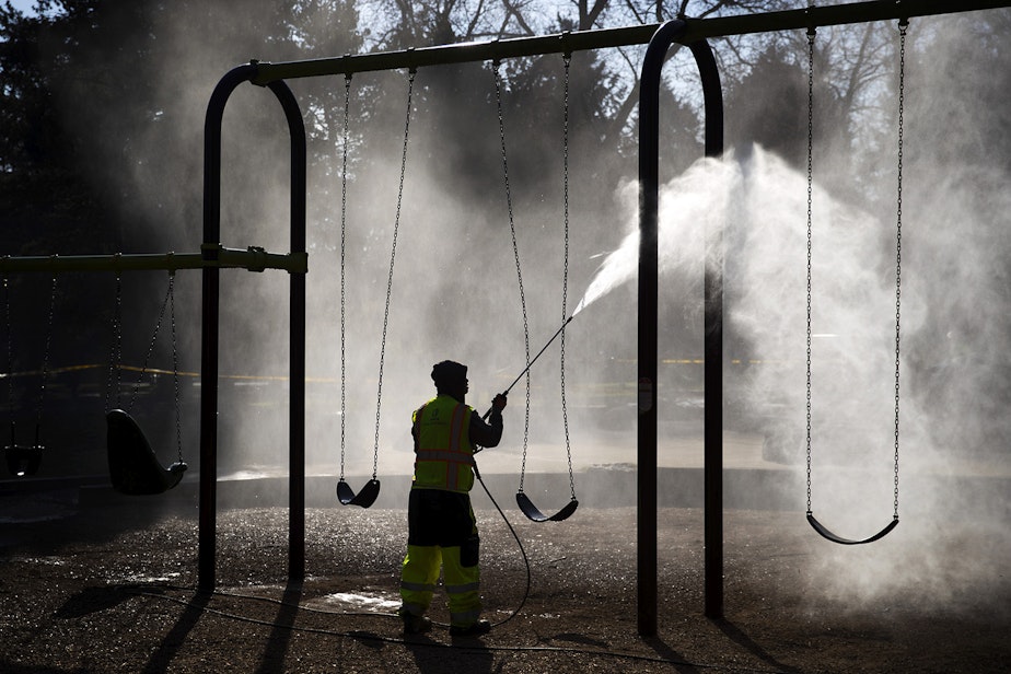 caption: Khai Tran, a utility worker with Seattle Parks and Recreation, sprays water onto a swing-set before a mixture of bleach and water is applied to the West Woodland Park Playground as a result of the coronavirus outbreak on Thursday, March 19, 2020, in Seattle.