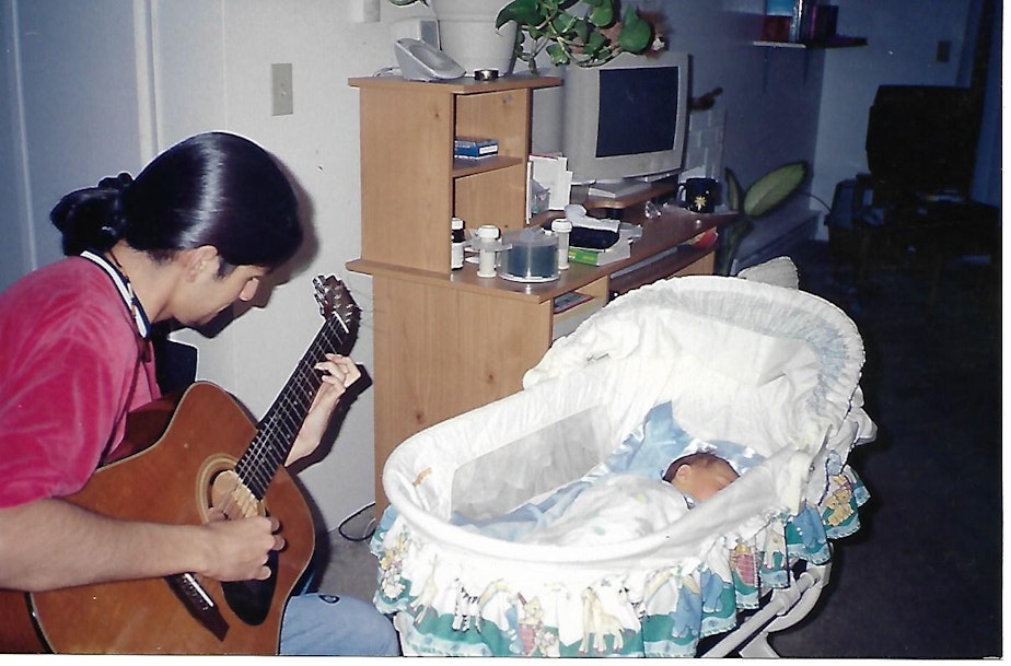 caption: Hugo Guerra plays a song on guitar to his newborn son Adrian Guerra, the author of this story, in their home in Everett.