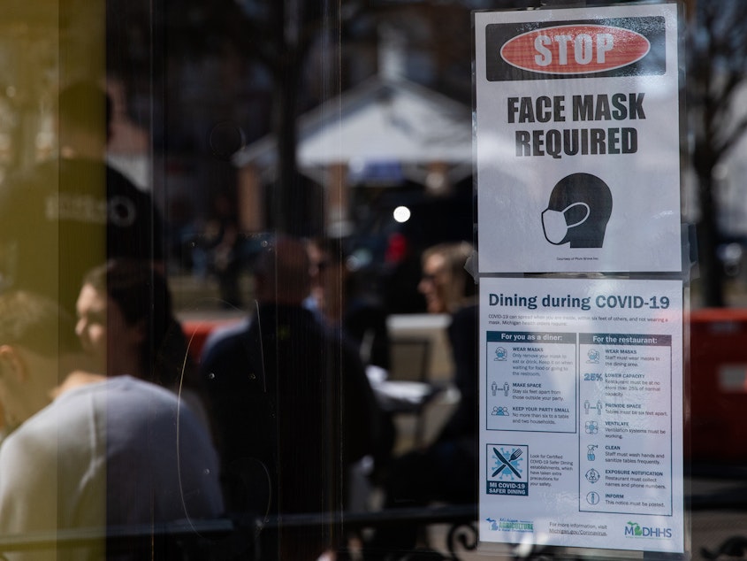 caption: A sign requiring face masks and COVID-19 protocols is displayed at a restaurant in Plymouth, Mich., on March 21. Coronavirus cases in Michigan are skyrocketing after months of steep declines, one sign that a new surge may be starting.