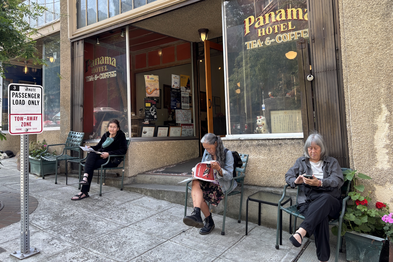 caption: Jan Johnson, owner of the Panama Hotel (on the left), and Leslie Morishita (center) read the newspaper on the sidewalk outside the historic Seattle hotel and tea house.