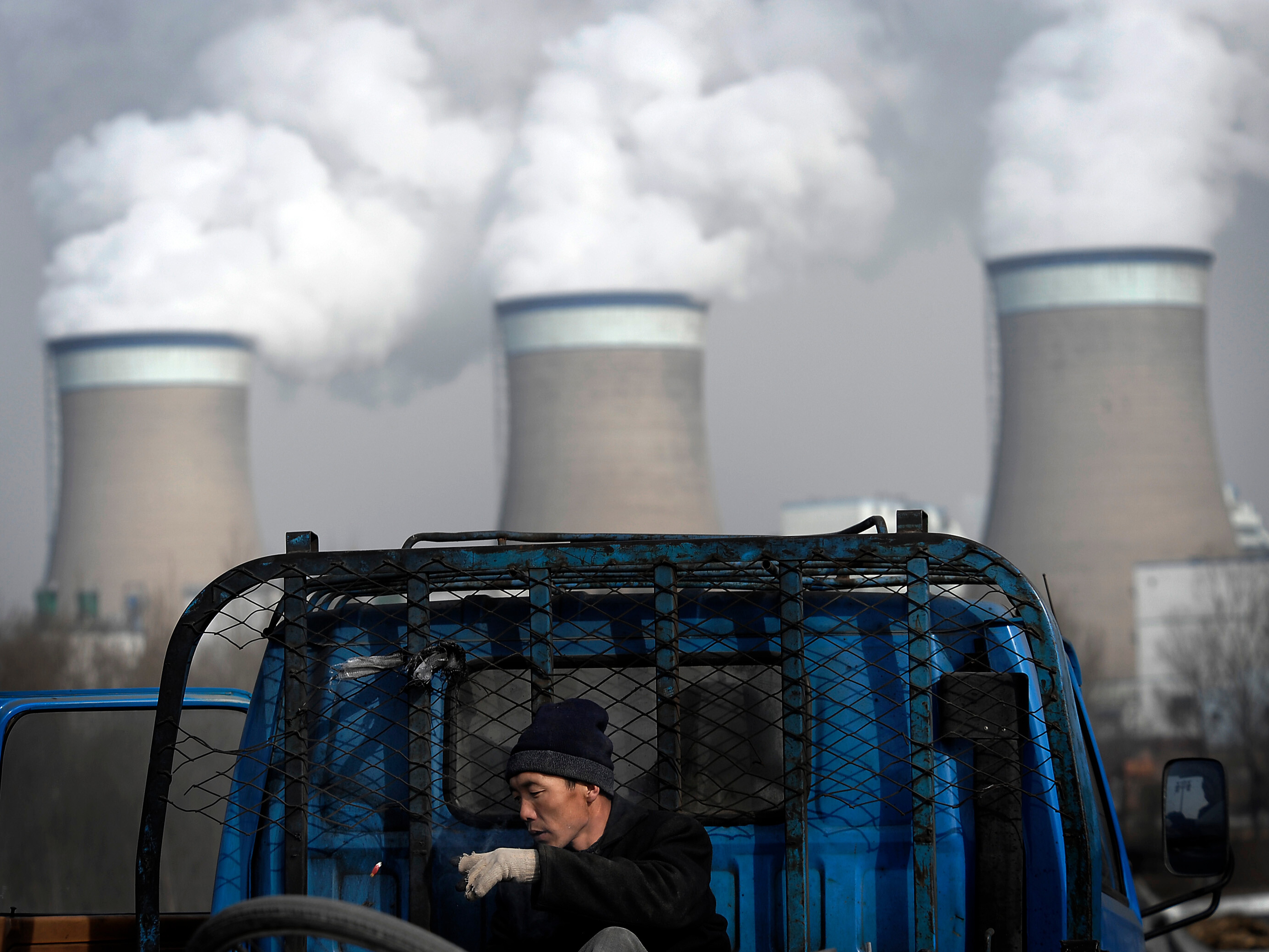 caption: FILE - A worker throws his cigarette on a truck parked in front of a cooling towers of a coal-fired power plant in Dadong, Shanxi province, China, on Dec. 3, 2009.