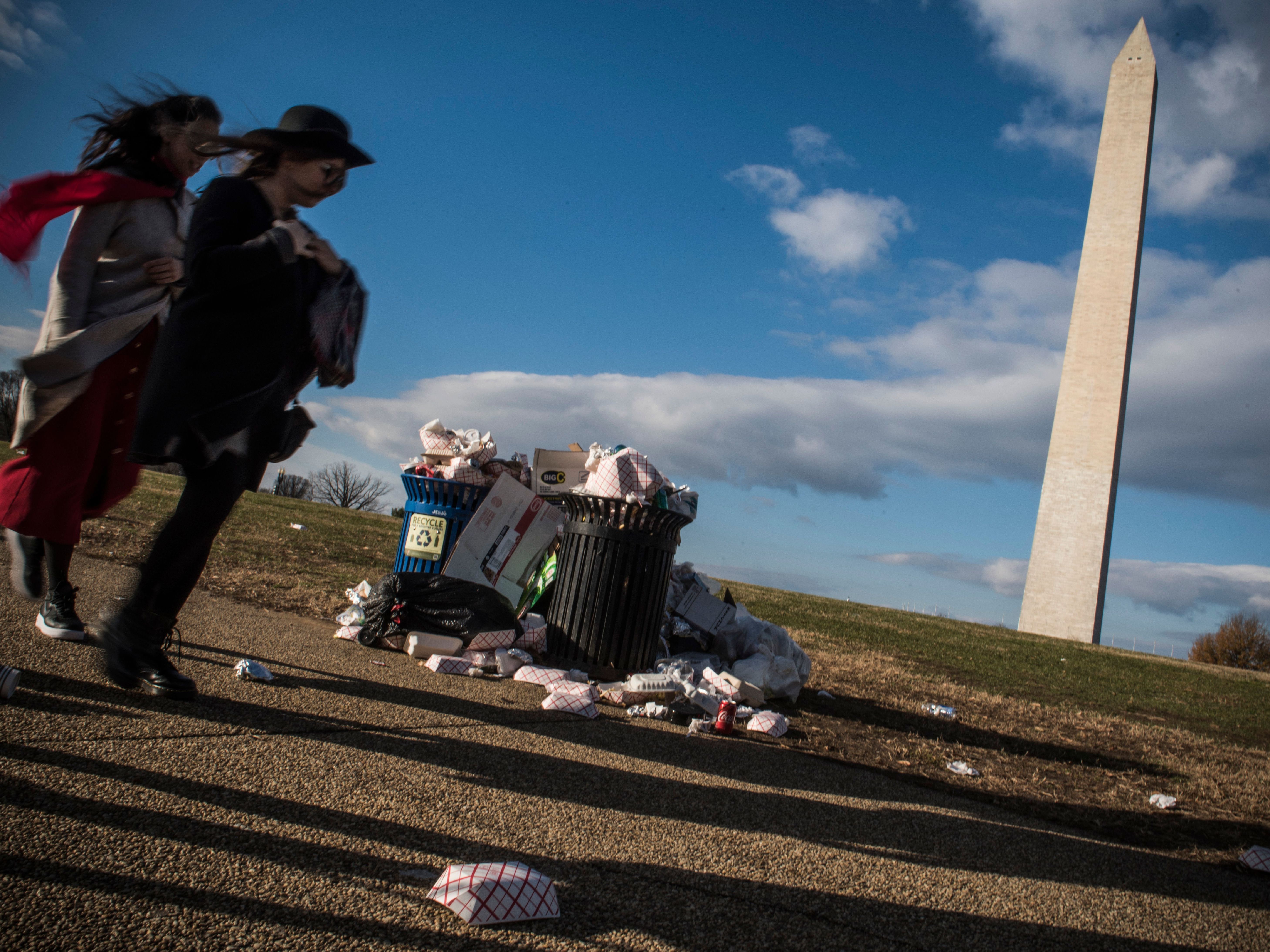 caption: Tourists walk past a public dustbin, spilling with litter, next to the Washington Monument on the National Mall in Washington, D.C. on Dec. 24, 2018.