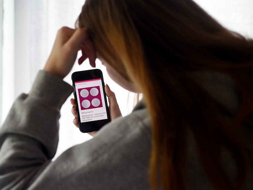 caption: In this photo illustration, a person looks at an abortion pill (RU-486) for unintended pregnancy from Mifepristone displayed on a smartphone on May 8, 2020, in Arlington, Va. Under federal law, even in states where telemedicine abortion is legal, there are strict rules surrounding how the pill is dispensed.