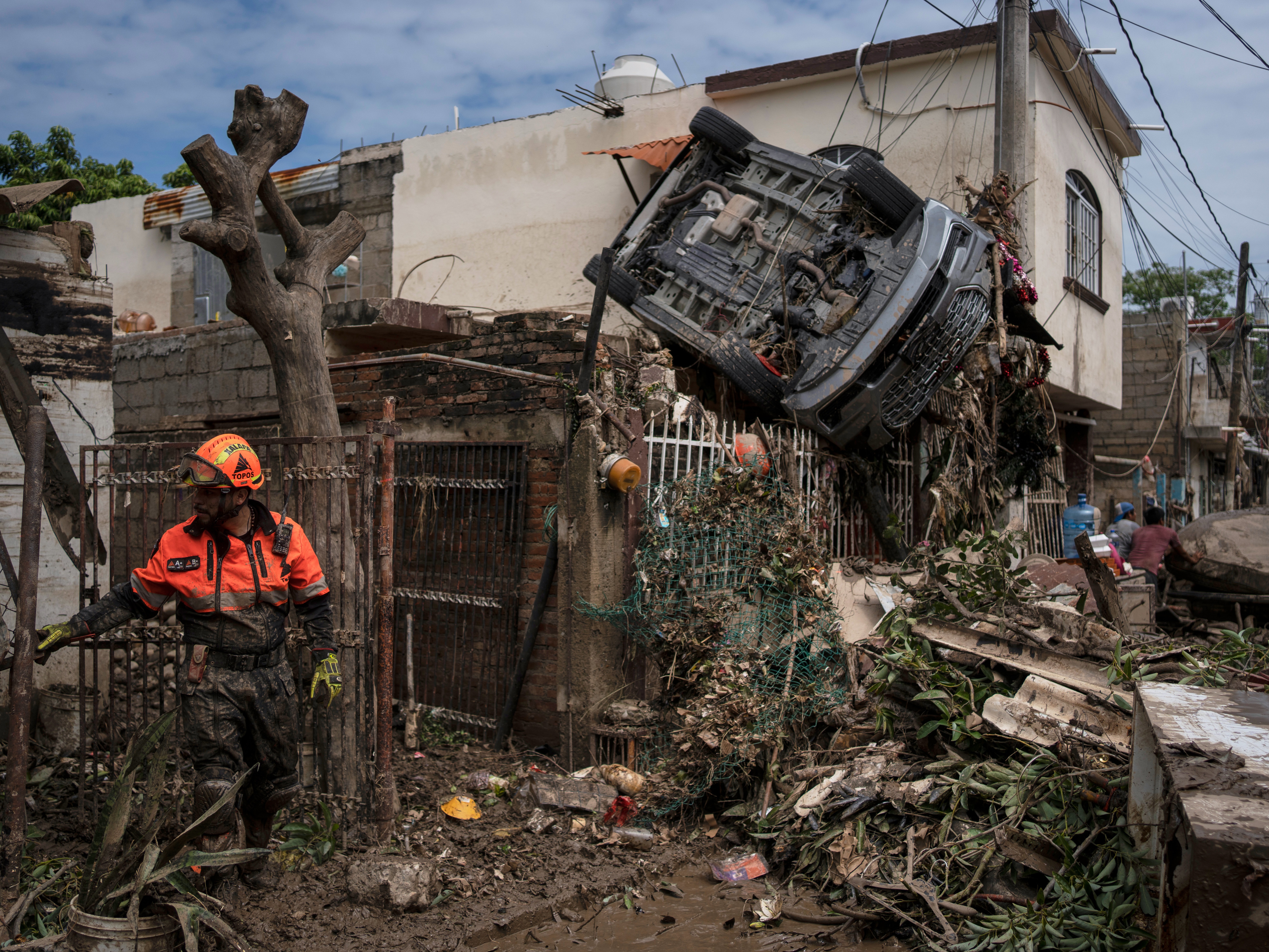 caption: A rescue worker, part of the volunteer brigade known as the Topos, works near a car hanging over a fence by a damaged house in Poza Rica, Mexico, Monday, Oct. 13, 2025, after torrential rains.