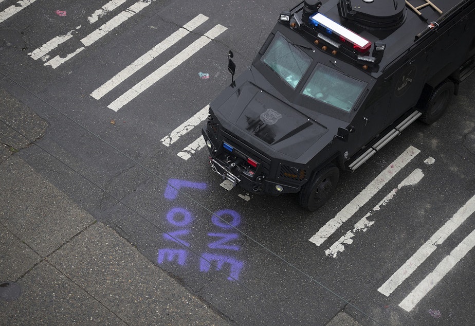 caption: An armored Seattle Police Department vehicle is parked at the intersection of 12th Avenue and East Pine Street, next to spray paint on the pavement reading 'One Love' after the Capitol Hill Organized Protest zone was cleared by Seattle Police Department officers early Wednesday morning, July 1, 2020, in Seattle.