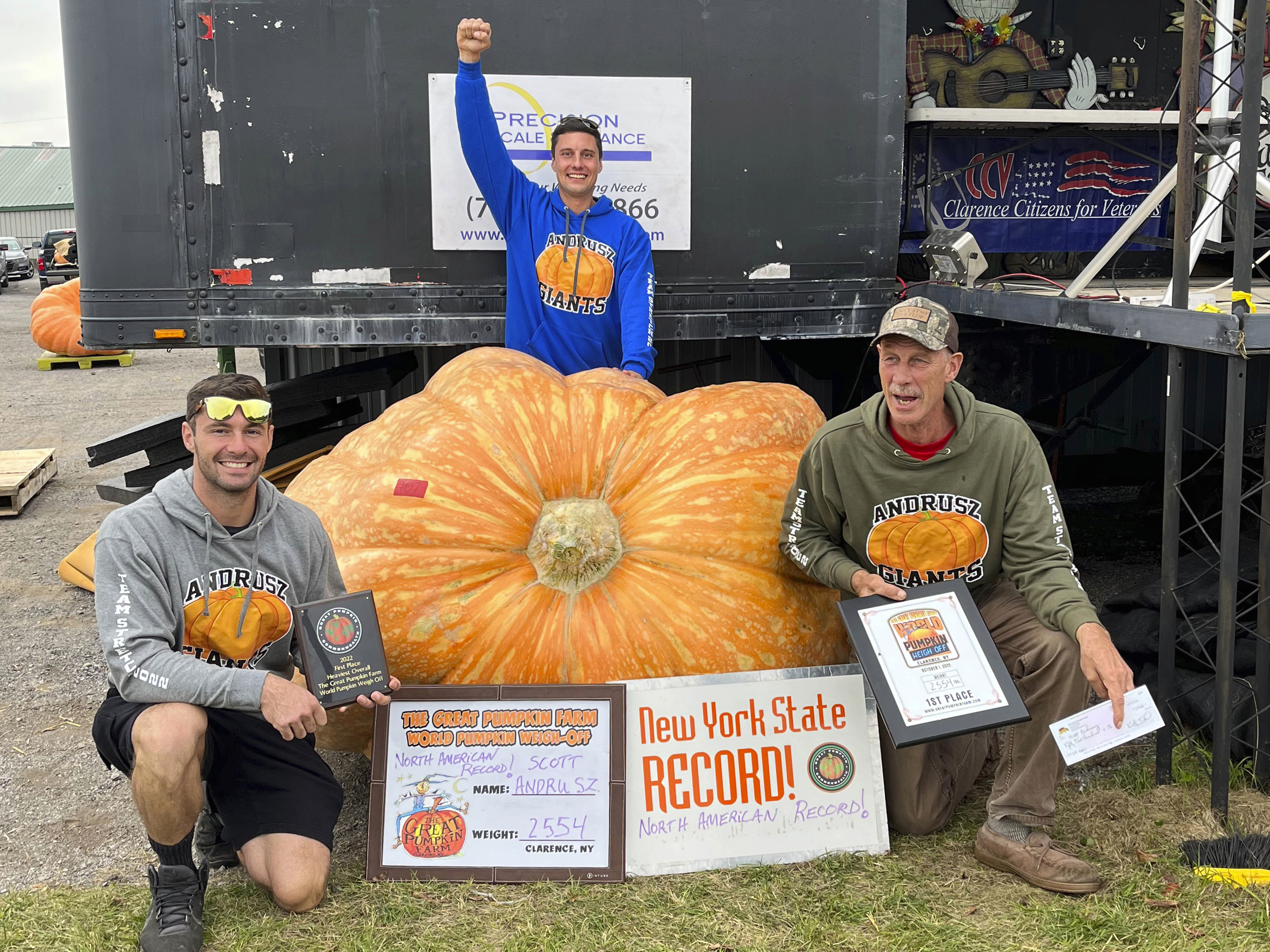caption: In this photo provided by The Great Pumpkin Farm, Emmett Andrusz, from left, Steve Andrusz and Scott Andrusz, pose with the record-setting 2,554-pound pumpkin in Clarence, N.Y., on Saturday.