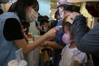 caption: Travel rules and regulations — and national lockdowns — have varied wildly, which gave SARS-CoV-2 lots of opportunities to spread. Above: A young traveler's temperature is checked at Taipei Songshan Airport in July 2020.