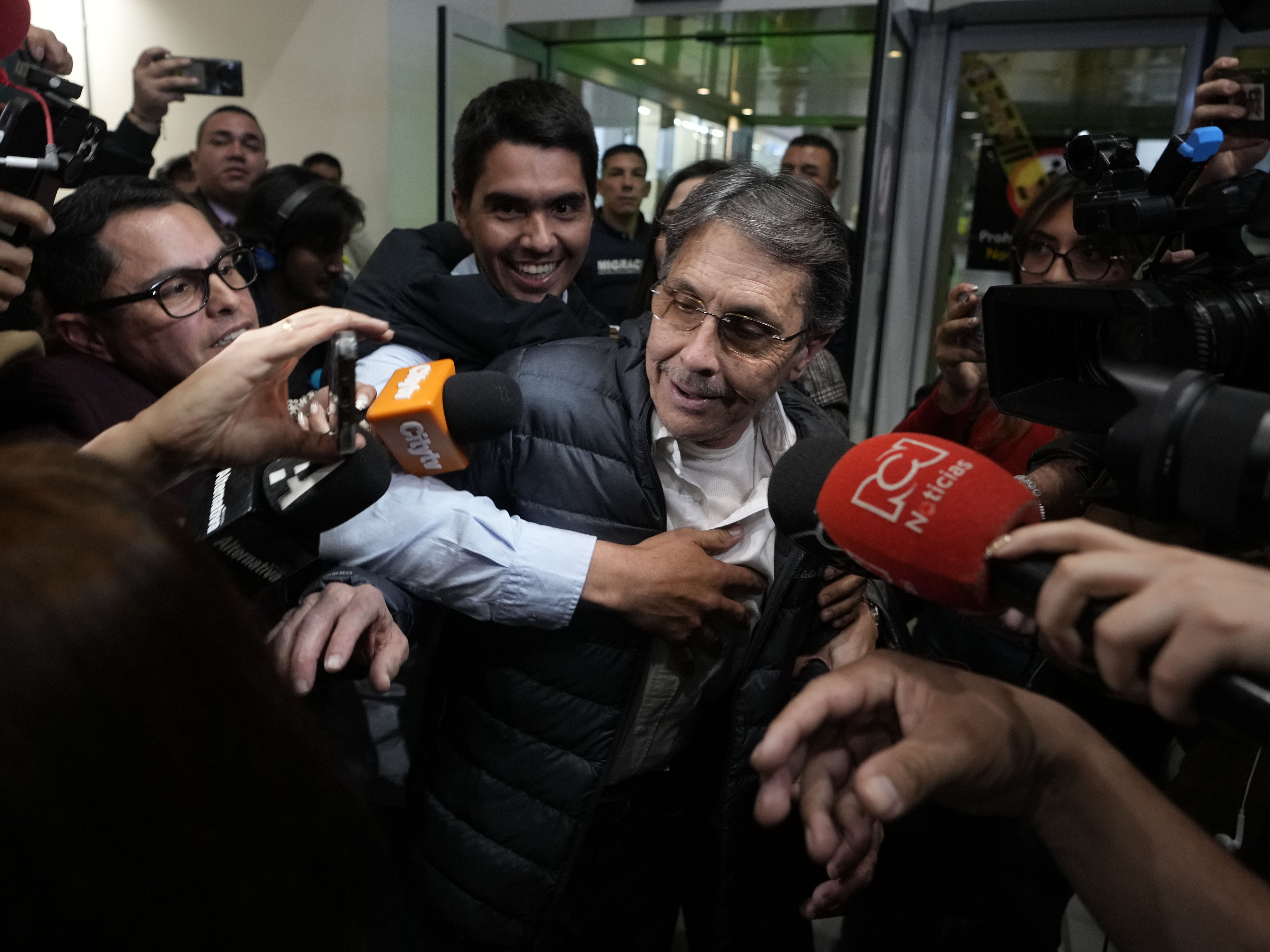 caption: Media swarm Fabio Ochoa, center, a former member of Cartel of Medellin, upon his arrival at El Dorado airport, after being deported from the United States, in Bogota, Colombia, on Monday.