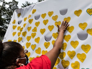 caption: COVID-19 survivors gather in New York and place stickers representing lost relatives on a wall in remembrance of those who have died during the pandemic.