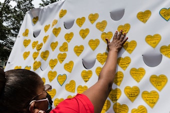 caption: COVID-19 survivors gather in New York and place stickers representing lost relatives on a wall in remembrance of those who have died during the pandemic.