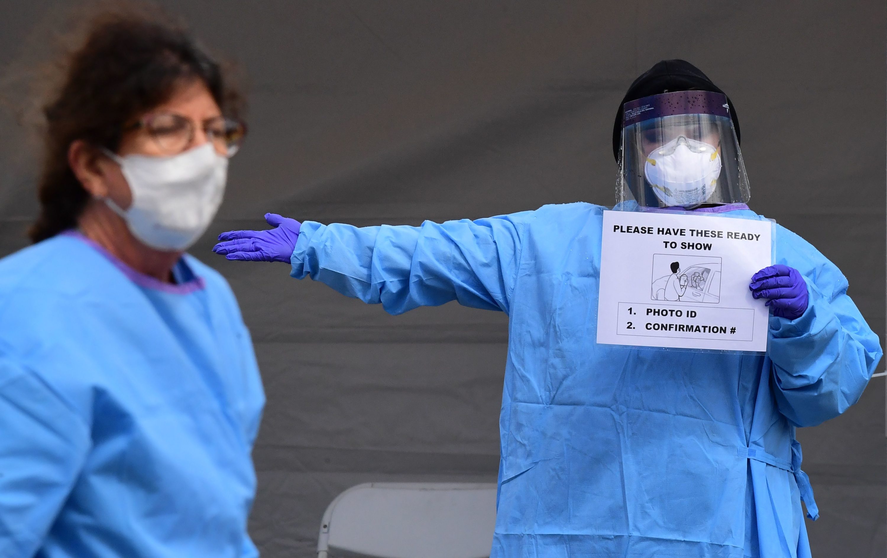 caption: Medical personnel wear facemasks and display instructions for people arriving in their vehicles for COVID-19 testing on April 8, 2020, on the first day of testing at the Charles R. Drew University of Medicine in south Los Angeles.(FREDERIC J. BROWN/AFP via Getty Images)