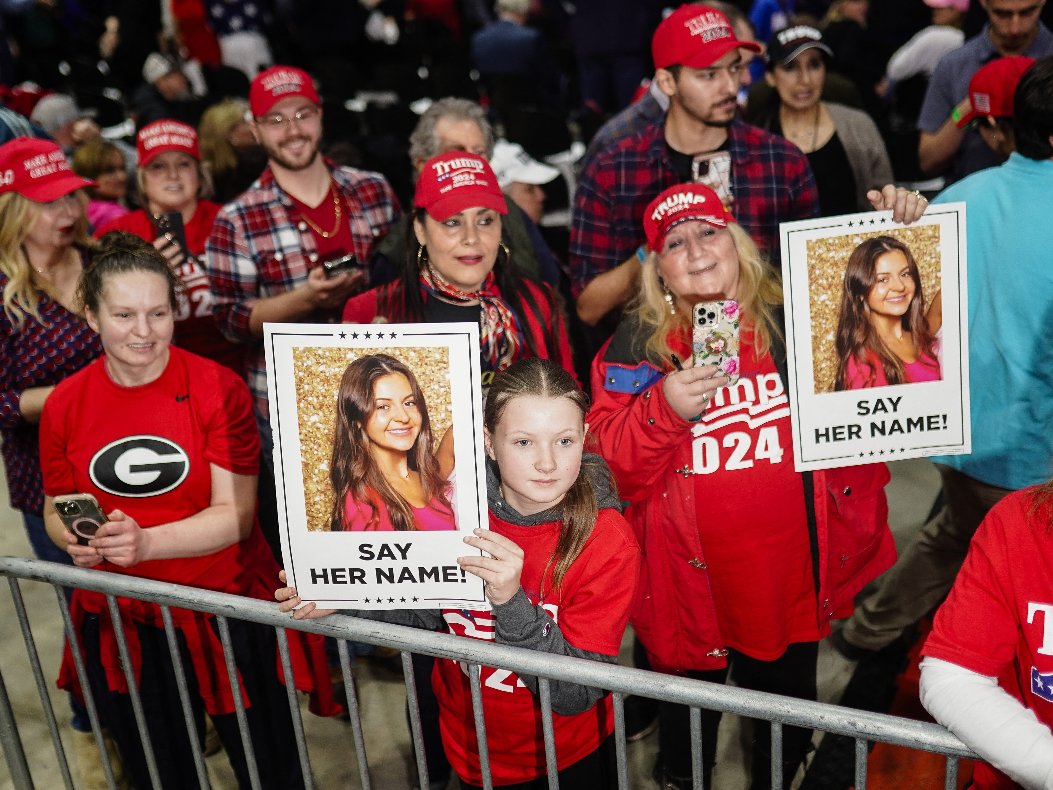 caption: Trump hold images of Laken Riley before he speaks at a rally in Rome, Ga., on March 9.